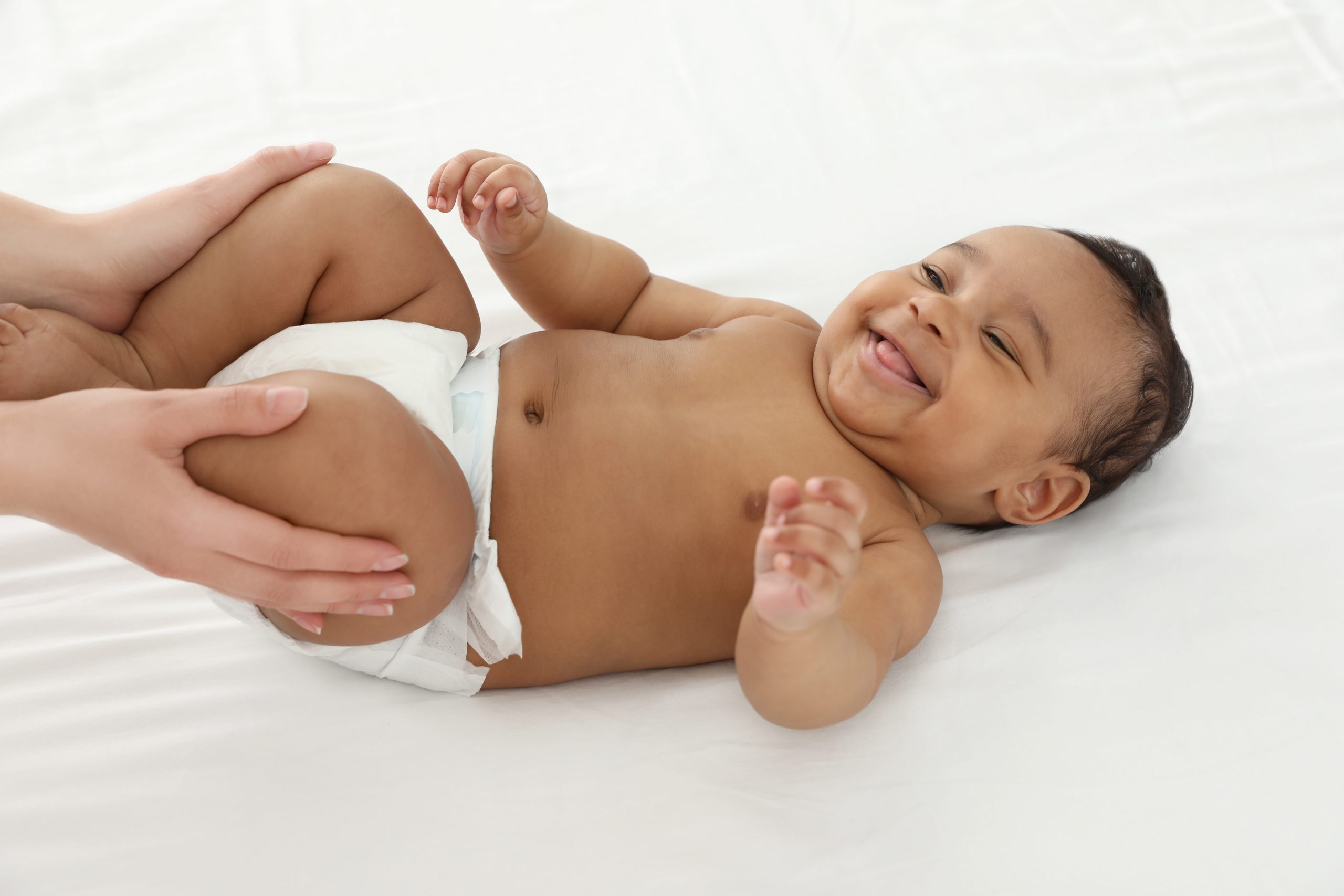 Bébé dans sa couche, allongé sur un lit qui rit avec Maman.